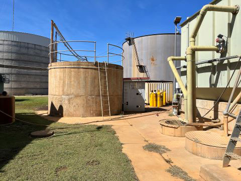 Several concrete water tanks with ladders and piping. There is grass and concrete in the foreground and blue sky above the tanks.