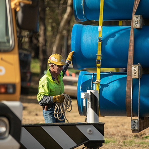 Man in hardhat and hi-vis vest checks pipelines before installation.