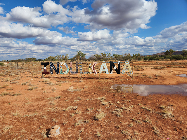 Photograph of an arid outback landscape with a multi-coloured Indulkana sign.