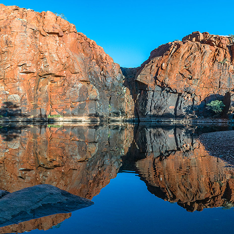 Python Pool in the Pilbara region of WA, with water in the foreground and large gorge rocks and blue sky in the background.