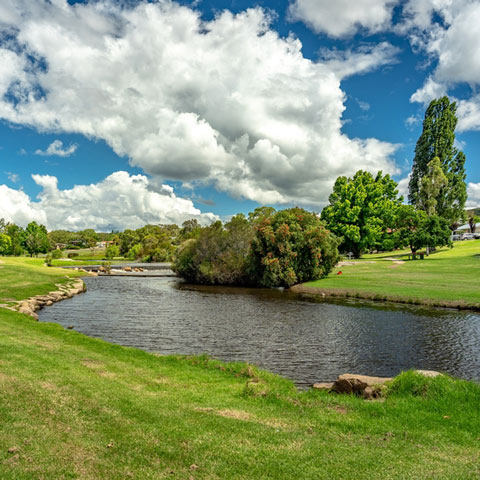 Creek surrounded by green grass with a blue cloudy sky.