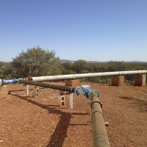 Water pipes in foreground with red, scrubby landscape.