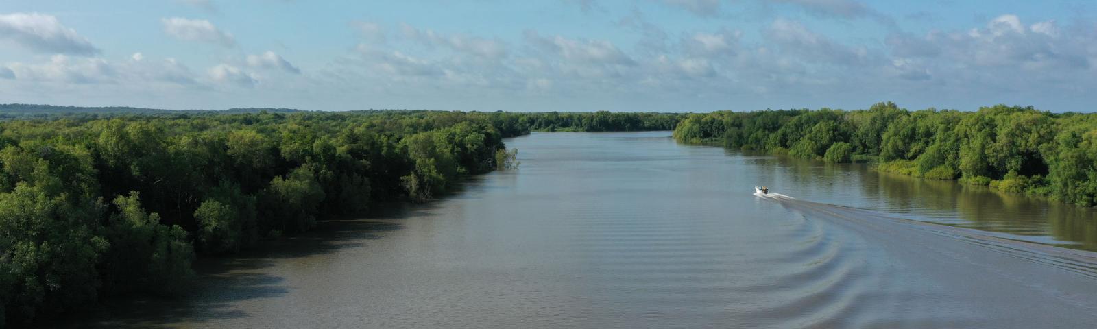 A boat is driving down a river with trees on either side.