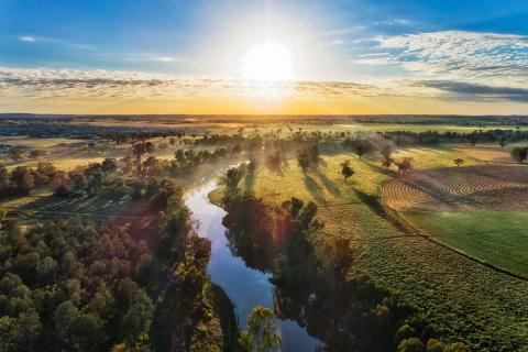 Sunrise over farmland with a winding river, open fields, and scattered trees.