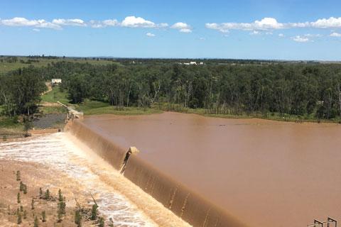 An overflowing weir with green bush in the background.