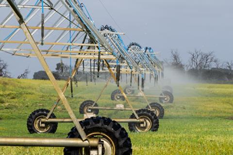 Sprinkler system in a green field with trees in the background and water mist in the air.