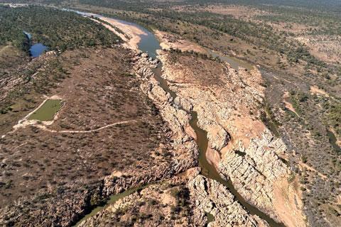 Ariel view of a water channel running surrounded by rocky ground and bushland.