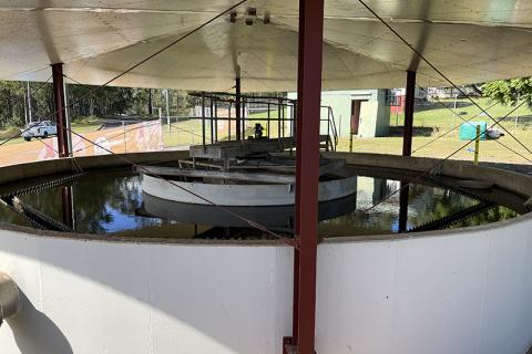 A large water clarification tank in Cherbourg’s Water Treatment Plant, filled with water. The tank structure is under a roof and is white and circular, surrounded by dark red poles.