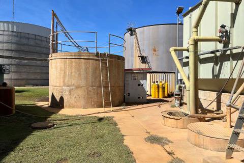 Several concrete water tanks with ladders and piping. There is grass and concrete in the foreground and blue sky above the tanks. 