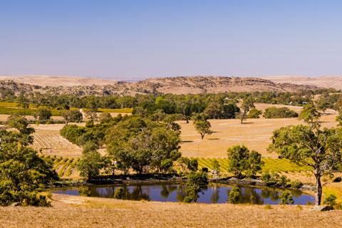 Photo of a dam and fields set against a blue sky.