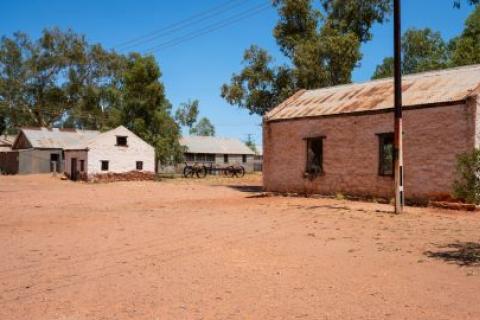 Landscape view of old Hermannsburg historic precinct in NT outback Australia – red dirt in the foreground and old buildings in the background.