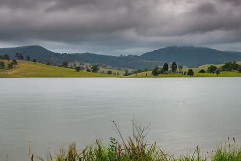 Lostock Dam with green grass in the foreground and green hills in the background with a cloudy sky above.
