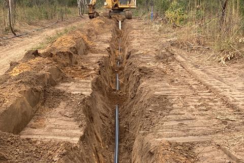A trench being dug by a crane in bushland.