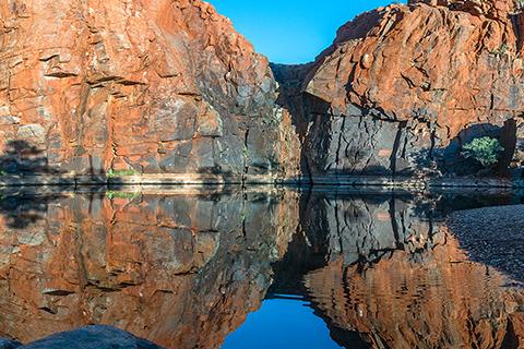 Python Pool in the Pilbara region of WA, with water in the foreground and large gorge rocks and blue sky in the background.