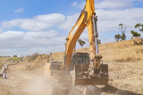Excavator clearing dry, dusty land.