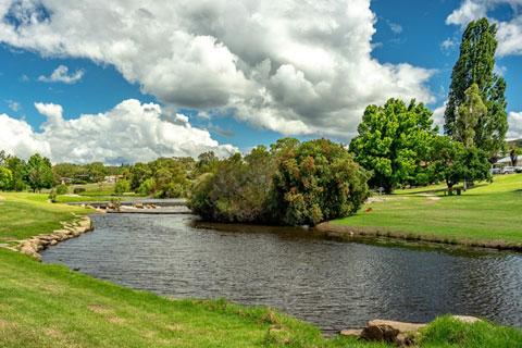 Creek surrounded by green grass with a blue cloudy sky.