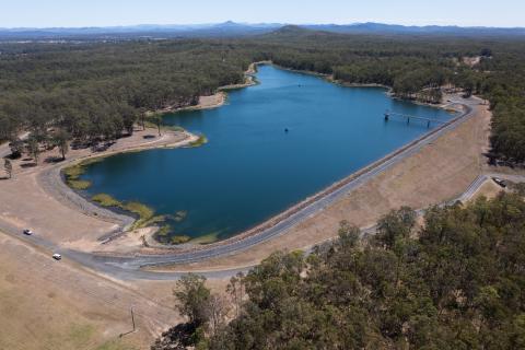 Photograph of an aerial view of Steuart McIntyre Dam filled with blue water and surrounded by green bushland.