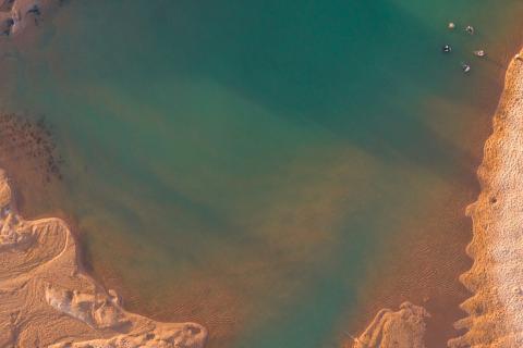 Aerial shot of a natural pool in a red sandy landscape.