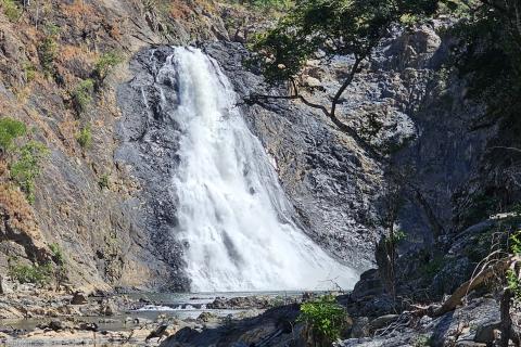 Waterfall surrounded by steep, dark, rocky cliffs and trees. There is a bright blue sky above the waterfall. 
