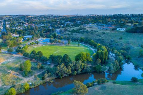 Aerial view of Yass River and township at sunset with green trees and grass on the bank of the river.