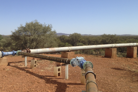 Water pipes in foreground with red, scrubby landscape.